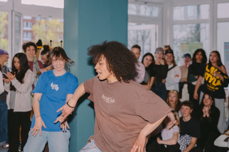 Zwei Personen tanzen zu Hip HOp. Im Hintergrund stehen und sitzen viele Menschen,